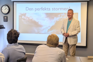 En man i vit kavaj, stående framför en storbildskärm